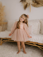 Eva tulle sleeve flower girl dress in champagne is worn by a young girl.