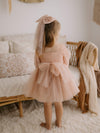 Eva flower girl dress in champagne is worn by a young girl along with a large tulle bow hair clip in champagne.