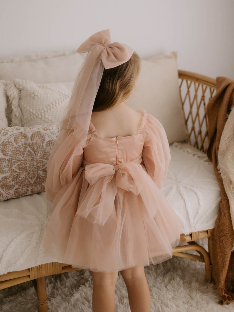 Eva champagne flower girl dress worn from the back, showing the tulle sash and matching champagne tulle bow hair clip.