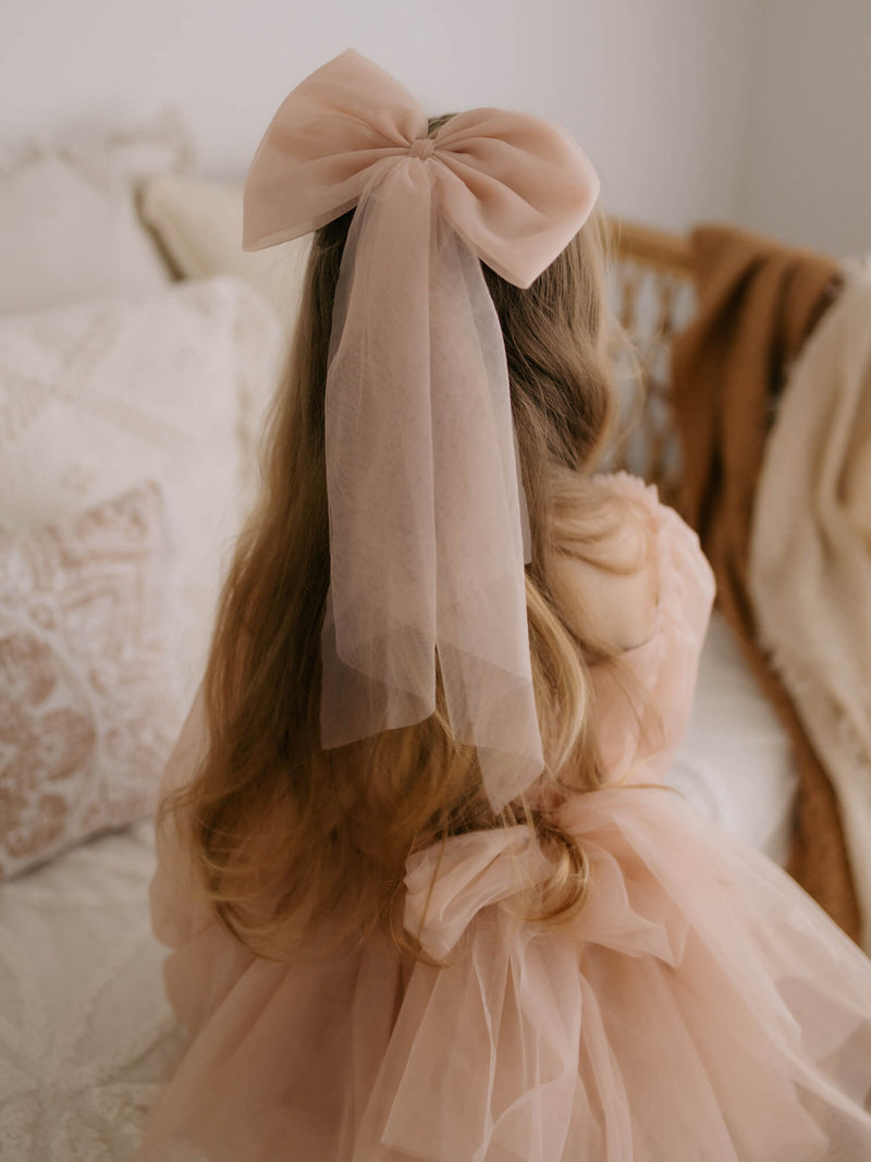 Large champagne tulle bow hair clip is worn by a young girl, along with our Eva champagne flower girl dress.