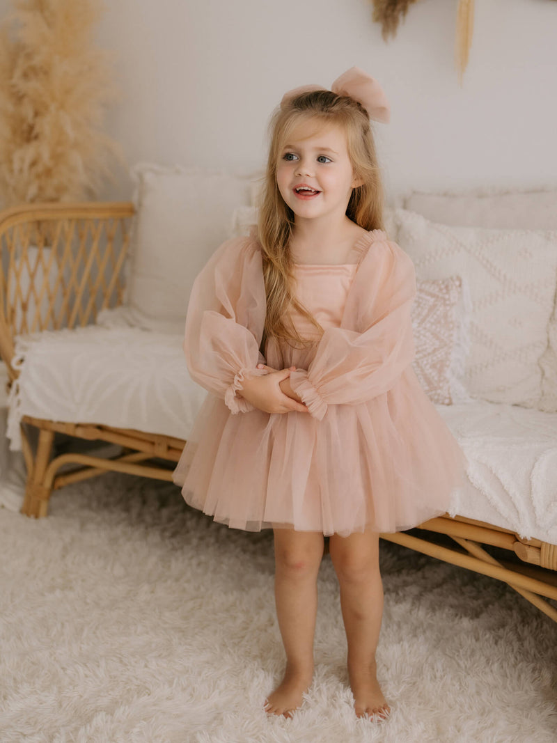 Eva flower girl dress in champagne is worn by a young girl, showing the full length tulle sleeves, satin bodice and tulle tea length skirt.