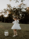 A young girl twirls in a field, wearing our Eva tea length tulle flower girl dress in ivory.
