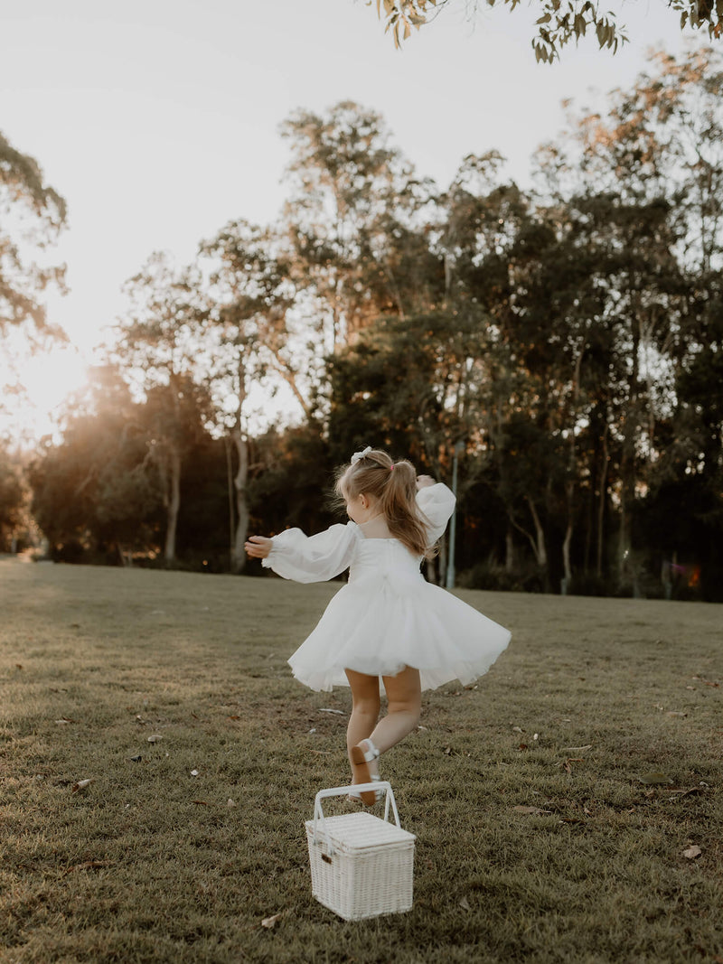 Flower girl twirls in a field wearing our Eva flower girl dress, showing the zip back, full length tulle sleeves and tulle bow tie at the back.