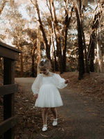 A flower girl walks down a path wearing our Eva ivory tulle flower girl dress and tulle bow hair clip.