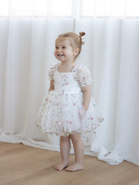 A toddler smiles wearing our Fleur meadow flower girl romper in meadow pink.