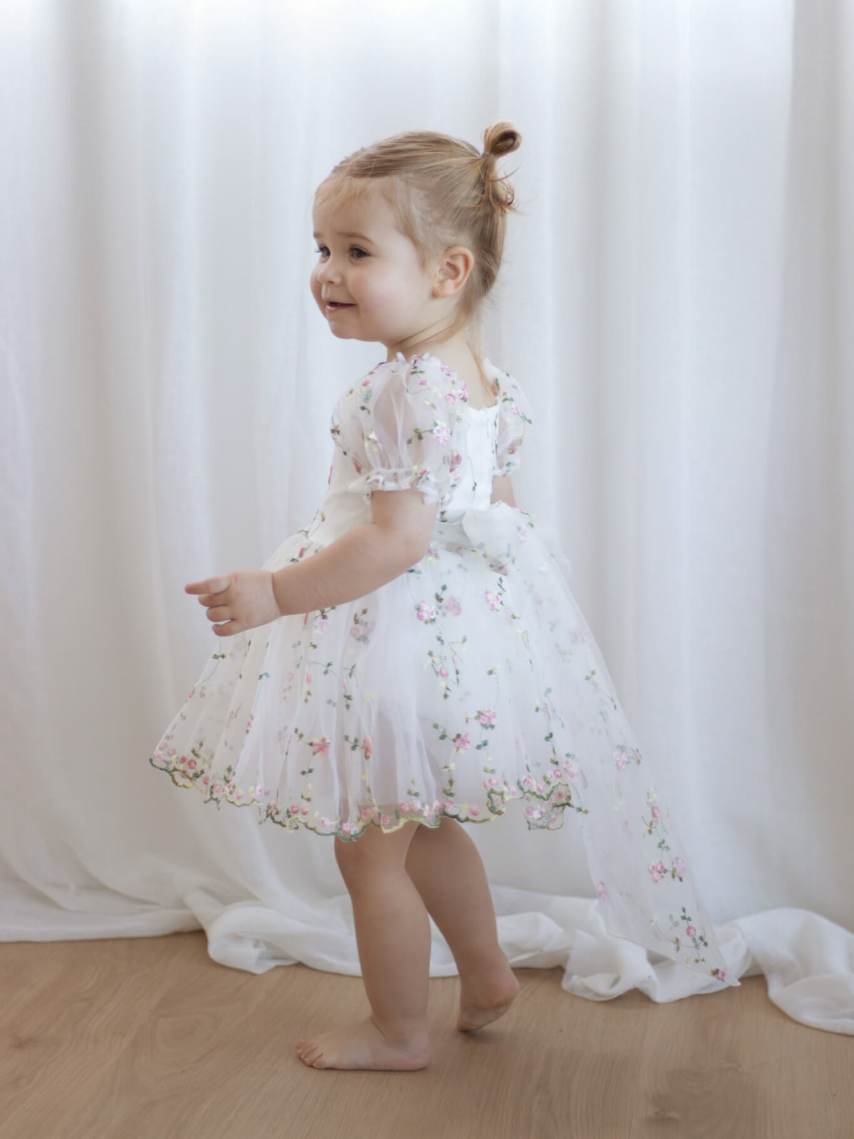 Fleur meadow pink flower girl romper is worn by a toddler, showing the organza bow at the back.