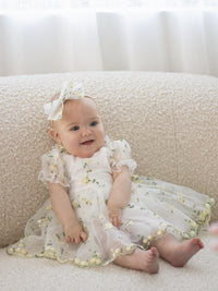 A baby smiles wearing our Fleur lemon blossom baby flower girl romper and matching bow headband.