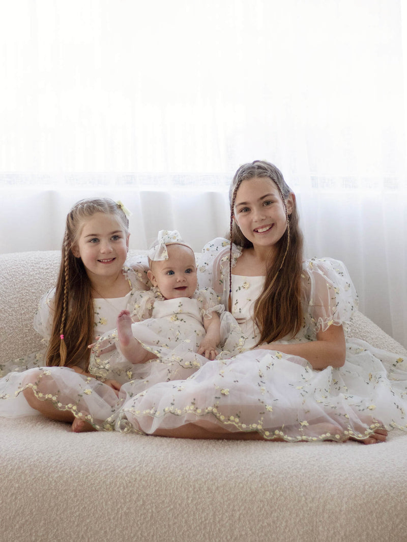Sisters sit wearing matching Fleur lemon blossom flower girl outfits.