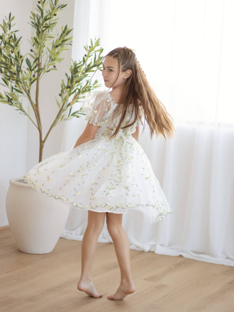 A young girl twirls, wearing our Fleur lemon yellow floral flower girl dress with puff sleeves.