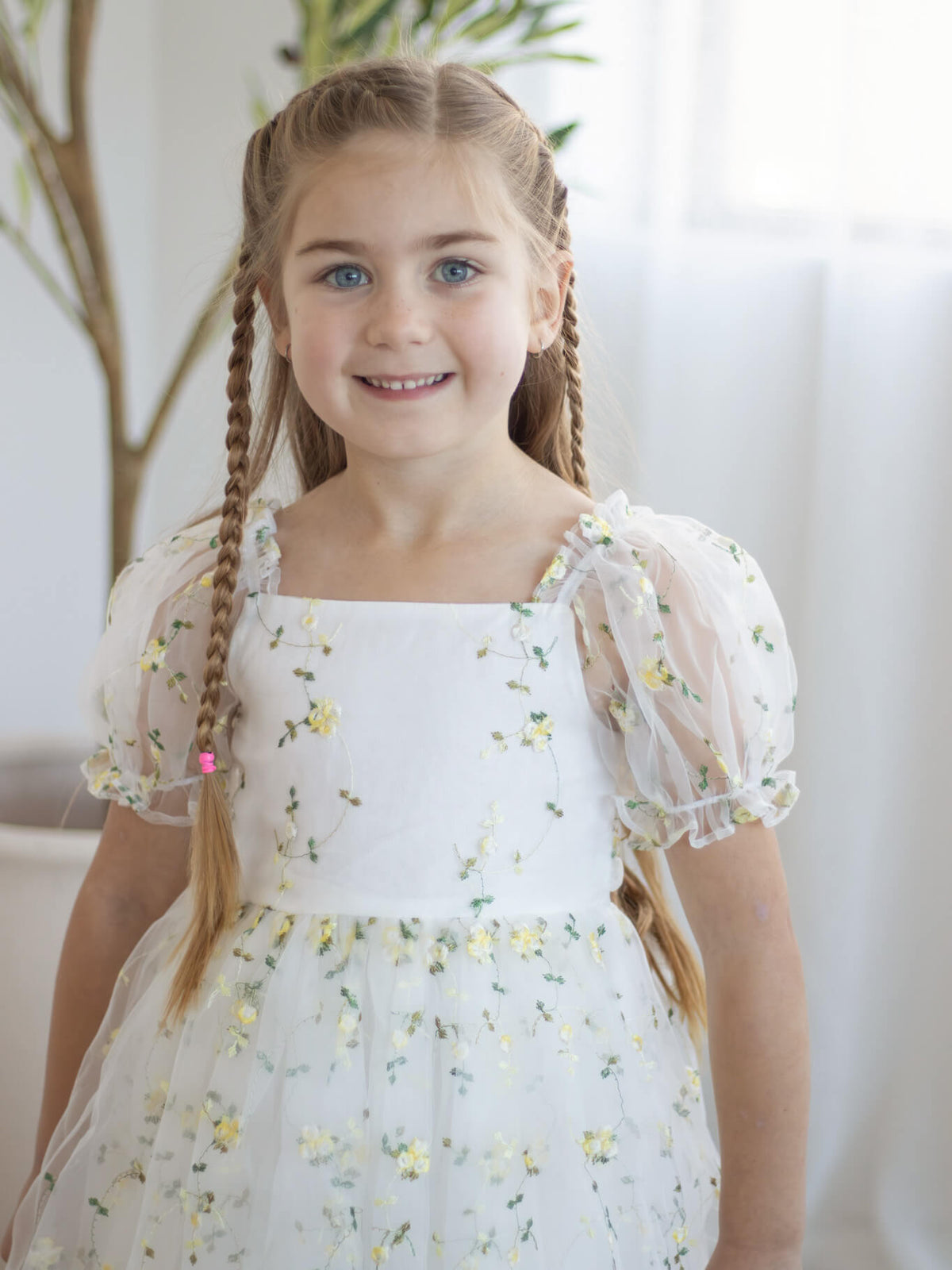 A young girl smiles wearing our Fleur lemon floral embroidered flower girl dress, with puff sleeves.