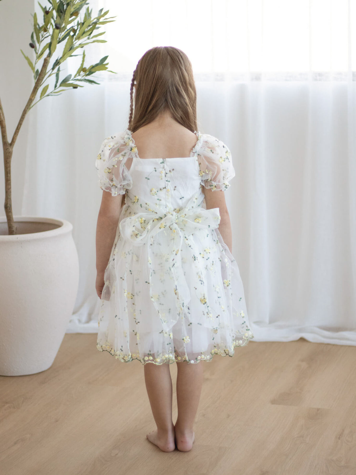 The back of our Fleur lemon blossom flower girl dress, showing the puff sleeves and organza bow at the back.