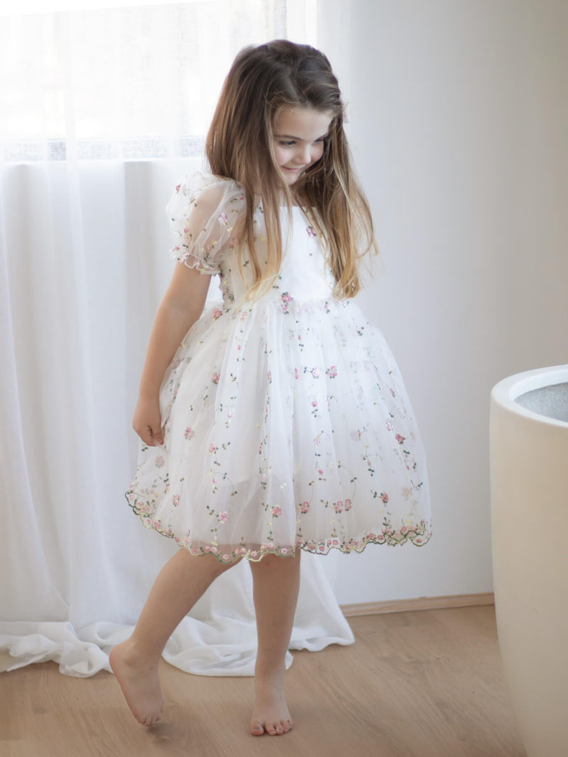 Young girl in a white and pink floral dress standing in a softly lit room.