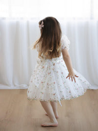 A little girl twirls wearing our Fleur flower girl dress in Meadow.