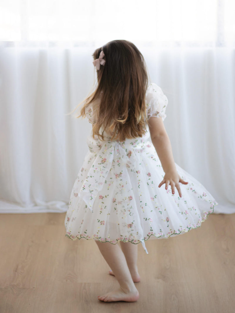 A little girl twirls wearing our Fleur flower girl dress in Meadow.