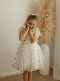 A little girl stands smiling, wearing our Fleur lemon floral flower girl dress.