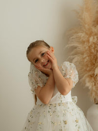A little girl smiling wearing our lemon floral flower girl dress, Fleur in lemon blossom.