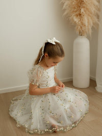 A little girl sits on the floor wearing our Fleur lemon blossom flower girl dress.