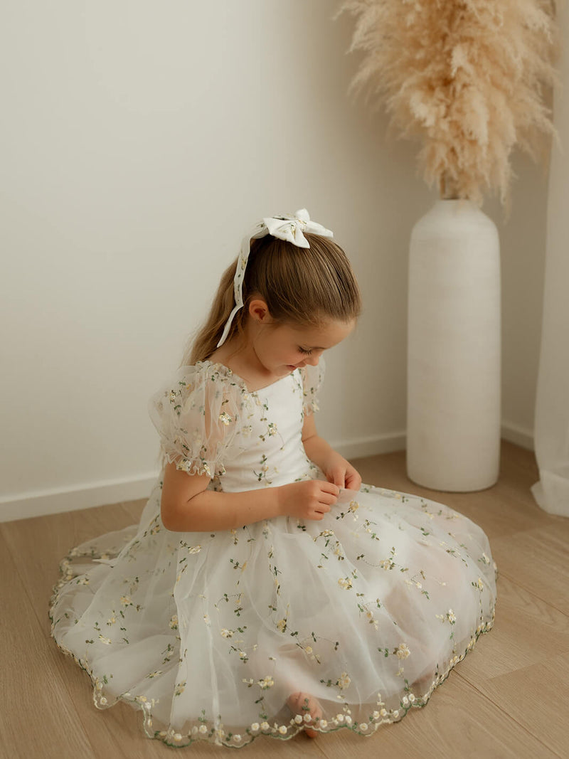 A little girl sits on the floor wearing our Fleur lemon blossom flower girl dress.