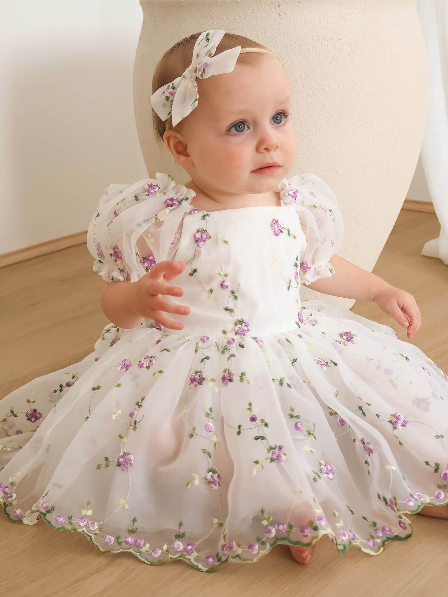 Fleur ivory and lilac baby flower girl romper is worn by a baby.
