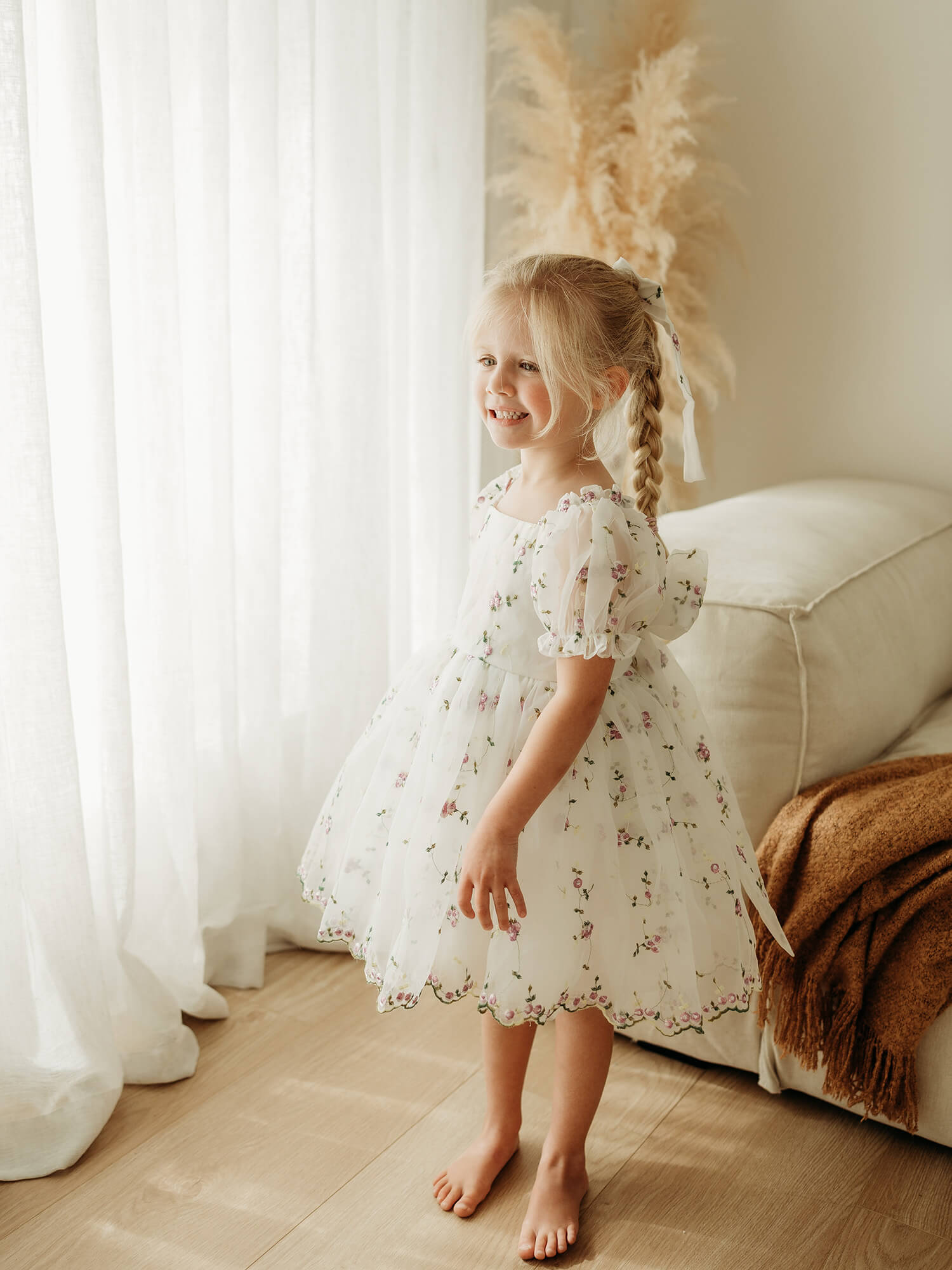 Fleur lilac floral flower girl dress is worn by a young girl, showing the organza puff sleeves and purple floral pattern.