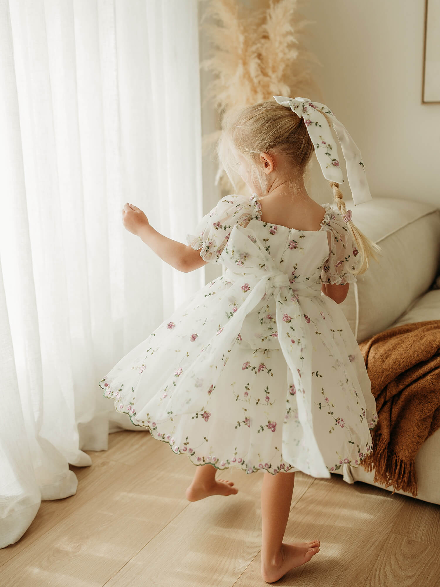 The back of our Fleur lilac purple flower girl dress, showing the organza bow at the back, is worn by a young girl who is dancing.