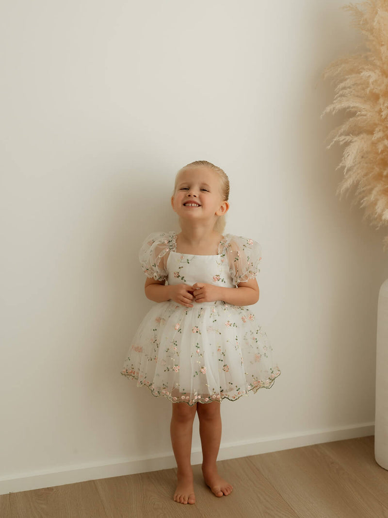 A little girl smiles, wearing our Fleur pink floral flower girl dress for babies and toddlers.