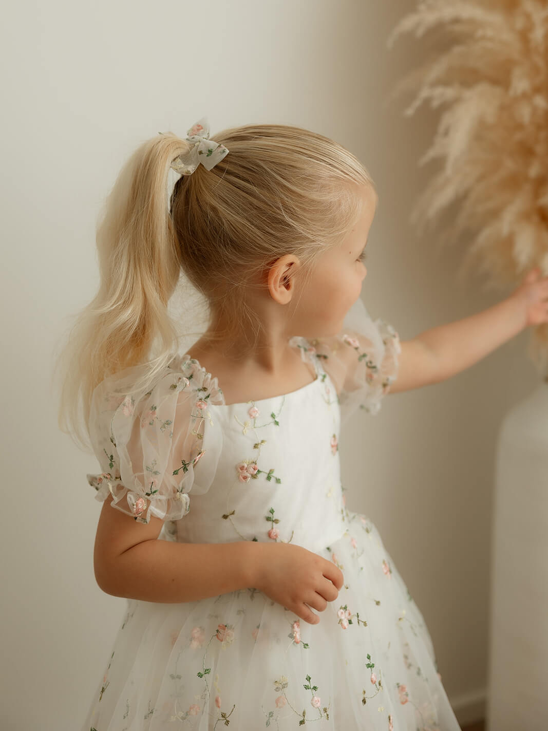 Our meadow floral baby flower girl romper and matching floral organza bow clip are worn by a young girl.