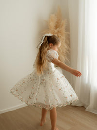 A young girl twirls wearing our Fleur flower girl dress in meadow pink, she also wears our matching Fleur floral hair bow.