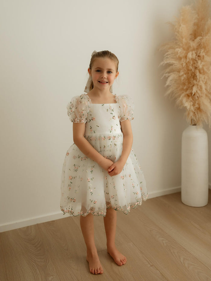 A young girl wears our Fleur meadow pink floral flower girl dress with puff sleeves.
