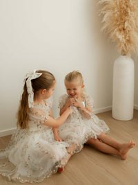 Sisters play wearing matching pink floral flower girl outfits.