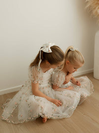 Sisters hug wearing matching floral flower girl dresses.
