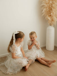 Sisters sit wearing matching Fleur meadow flower girl dress and Fleur meadow flower girl romper.