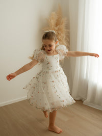 Young girl in our Fleur floral flower girl dress dancing in a room with white walls and curtains.