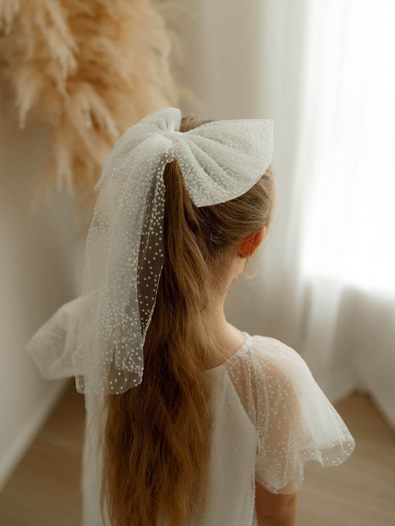Child wears our Gia flower girl dress and matching ivory flocked confetti tulle bow.