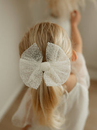 Medium flocked confetti tulle bow in ivory is worn by a young girl with blonde hair.