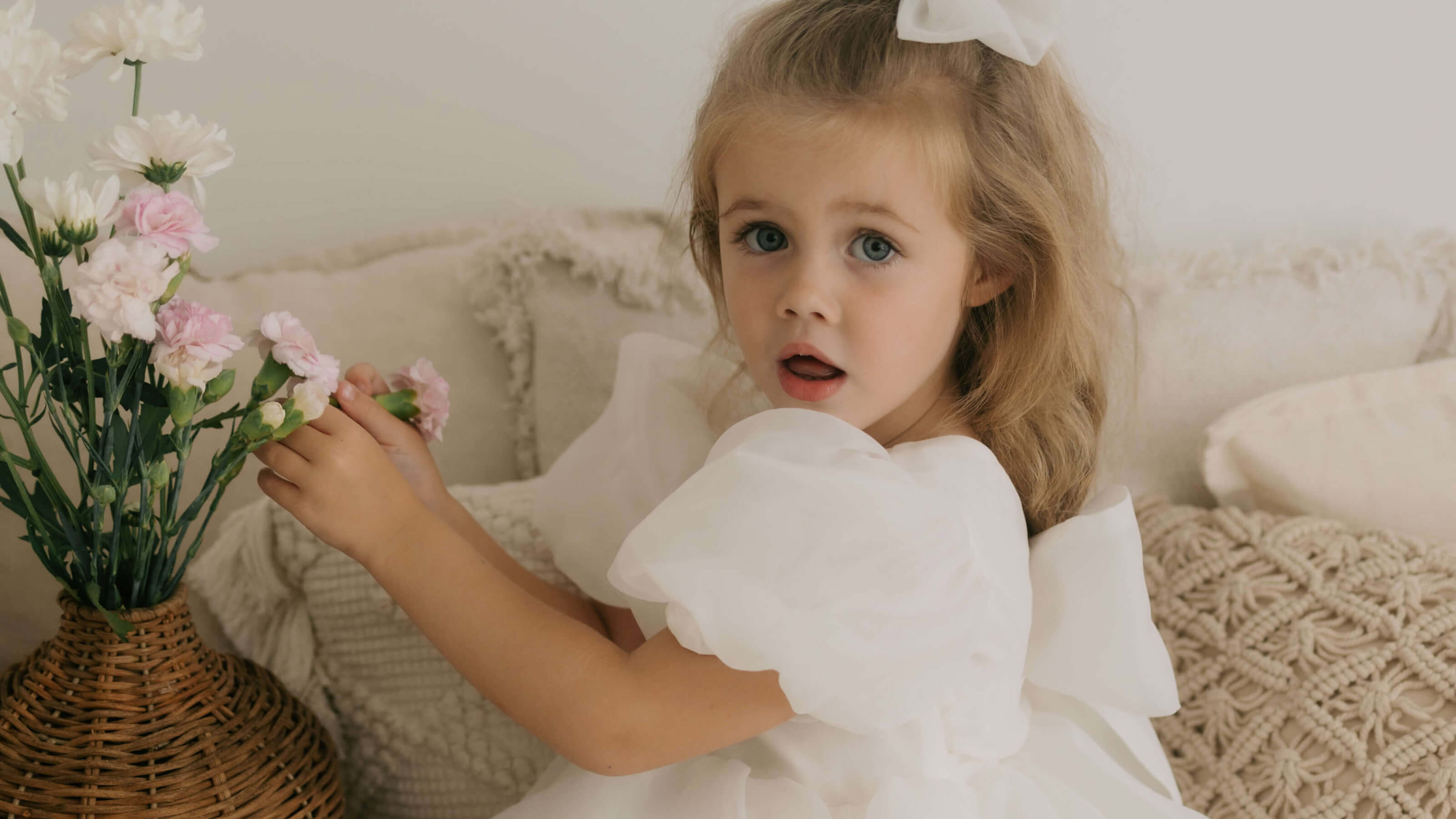 White flower girl dress with puff sleeves worn by a young girl holding flowers.