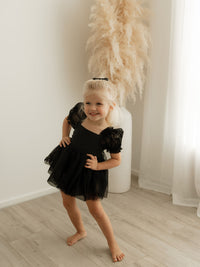 A toddler dances wearing our black baby flower girl romper.