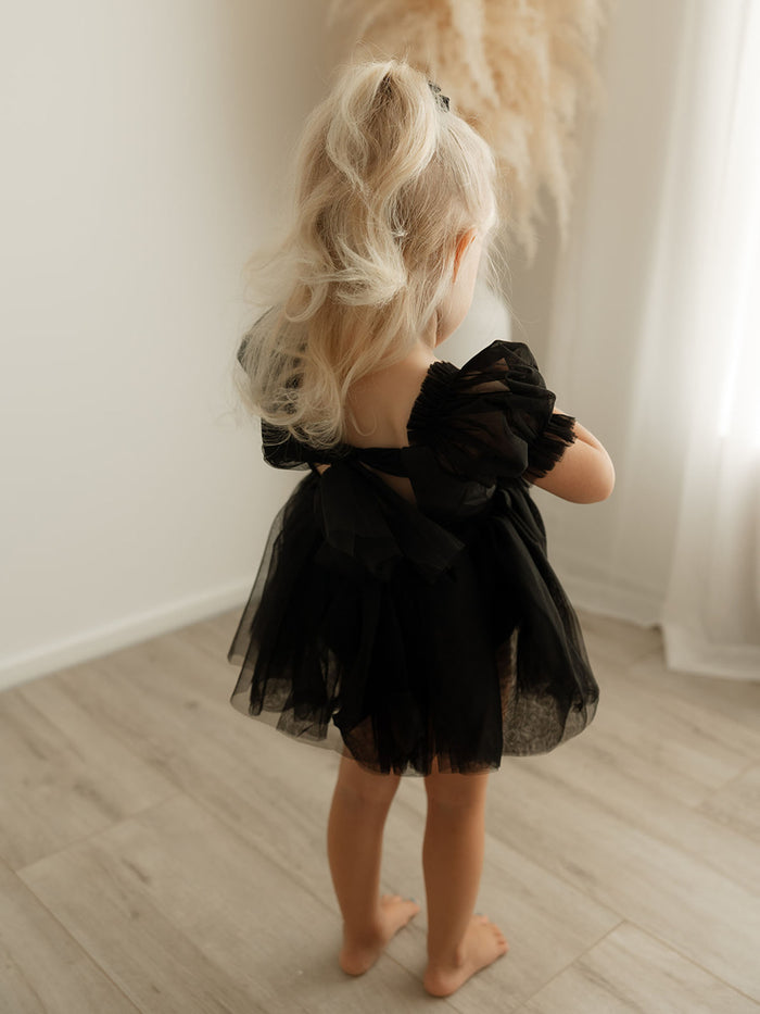 Gabrielle black flower girl romper for babies is worn by a toddler, showing the black tulle bow at the back.