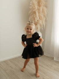 Gabrielle black baby romper with tulle puff sleeves is worn by a toddler.