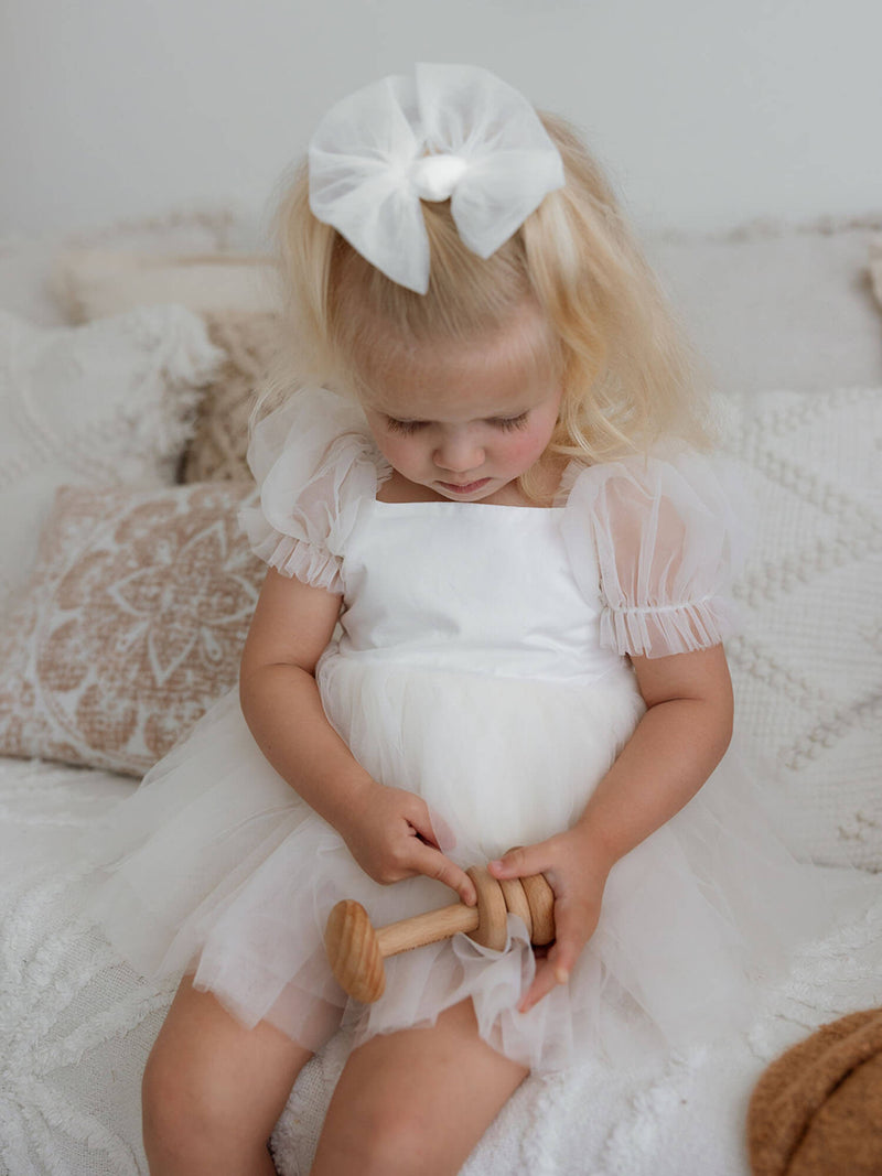 Close-up of a toddler playing with a wooden toy, dressed in our Gabrielle cream baby flower girl outfit with tulle sleeves.