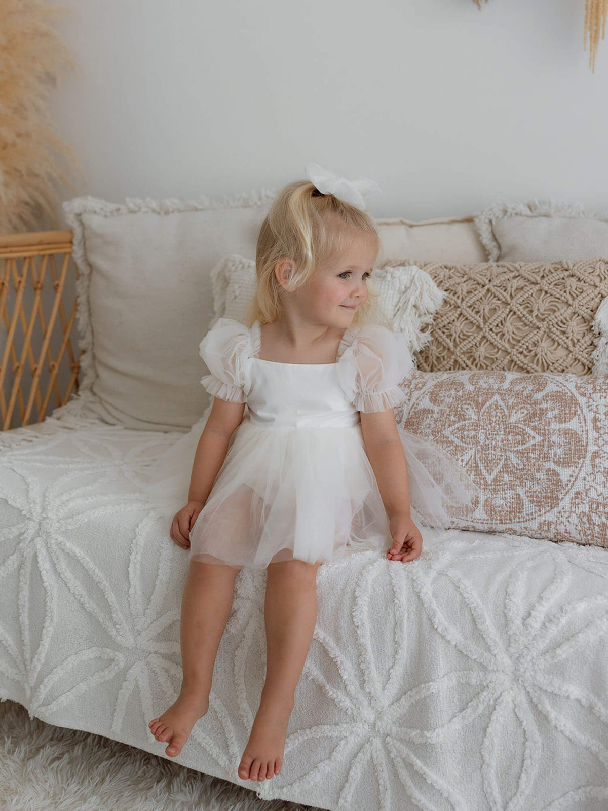 A toddler sits wearing our Gabrielle cream tulle baby flower girl dress.