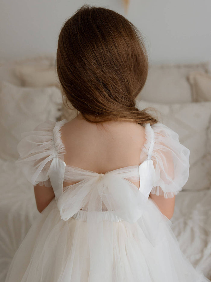 Our Gabrielle cream flower girl dress is worn by a young girl, showing the large tulle bow at the back.