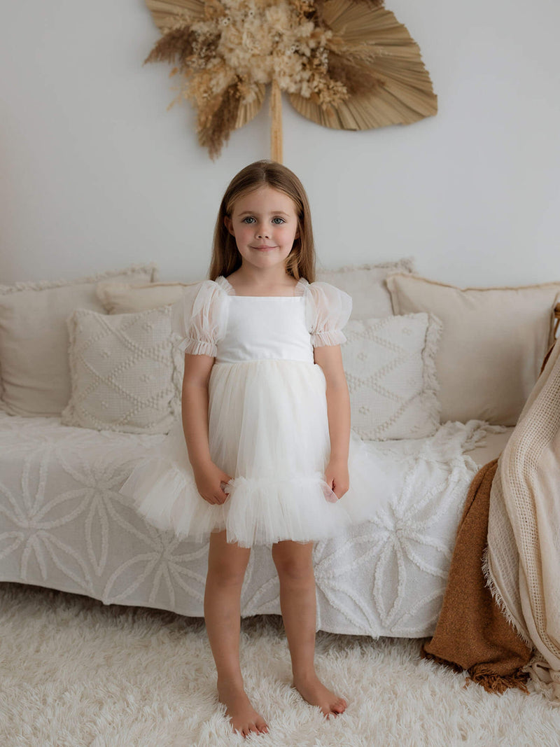 A young girl standing in our Gabrielle cream tulle flower girl dress with tulle puff sleeves.