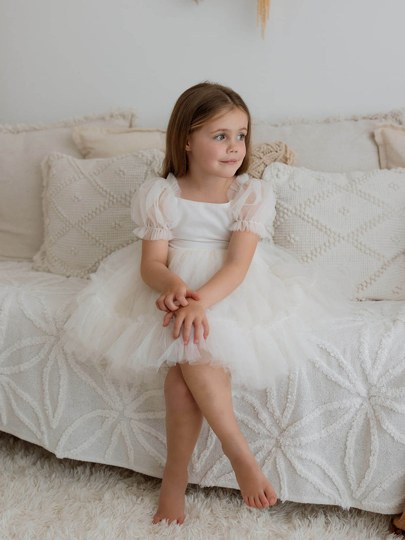 A young girl sits wearing our Gabrielle cream tulle flower girl dress.