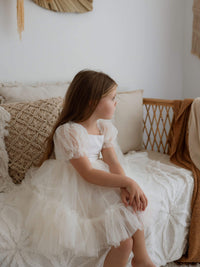 A young girl sits wearing our Gabrielle tulle puff sleeve flower girl dress in cream.