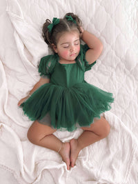 A sleeping toddler wears our Gabrielle baby flower girl romper dress in emerald green. She also wears matching green tulle bows in her hair.