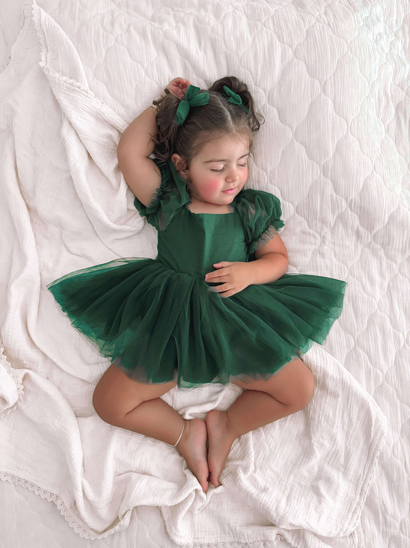 A smiling sleeping toddler wears our Gabrielle emerald green flower girl romper dress.