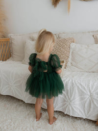 Green flower girl romper dress is worn by a toddler, showing the tulle bow at the back.