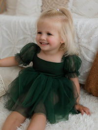 A toddler sits in our Gabrielle baby flower girl dress in emerald green.