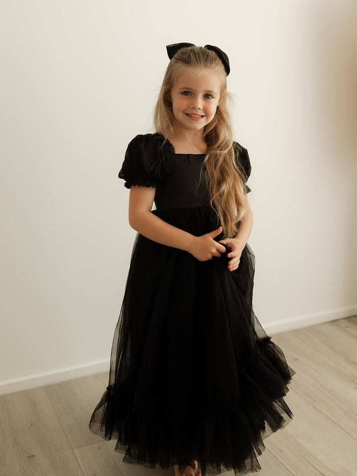 Gabrielle black flower girl dress is worn by a young girl. She also wears a matching black tulle bow in her hair.